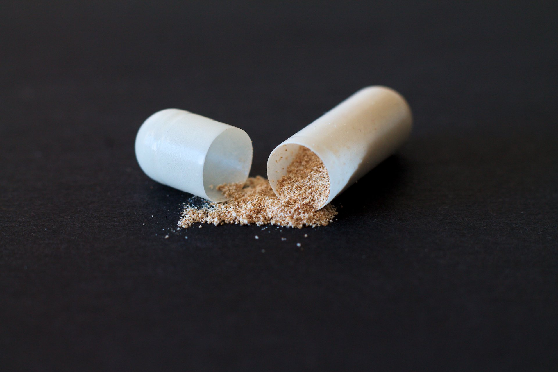 An opened capsule, its powder spilled on black
